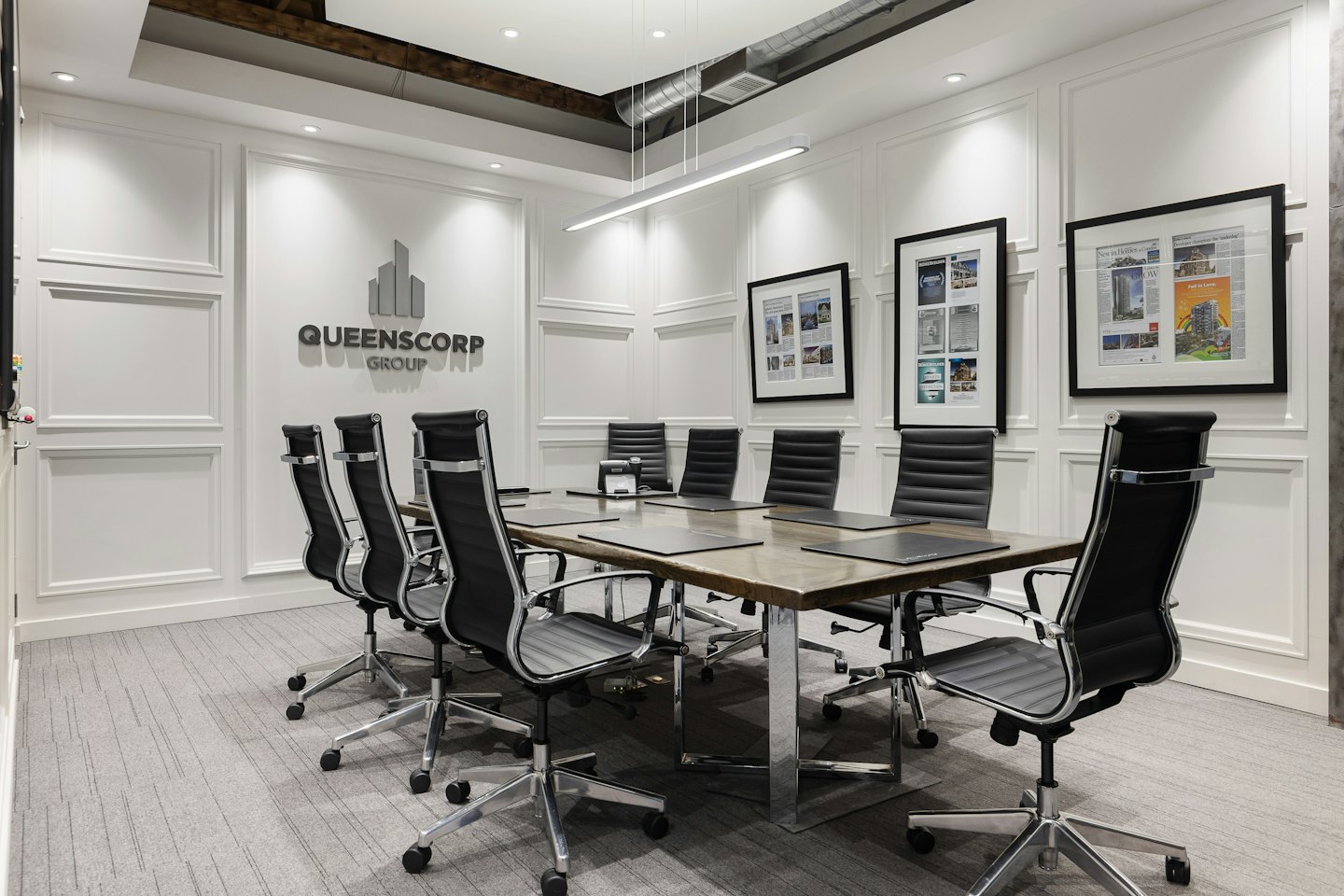 Sala konferencyjna z długim stołem i logo Queenscorp Group.
