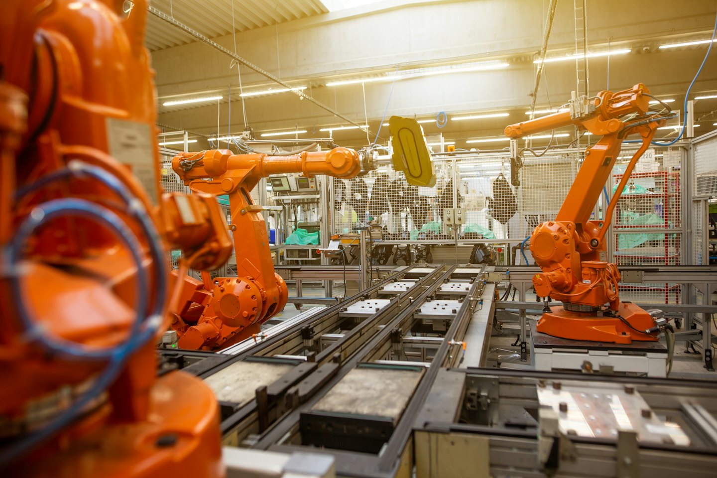 Robotyczne ramiona składają podzespoły na jasno oświetlonej hali produkcyjnej.
